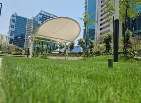 Curved white tensile canopy on arched steel legs in a landscaped garden