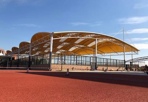 Long tensile membrane roof with a wavy edge over a sports court