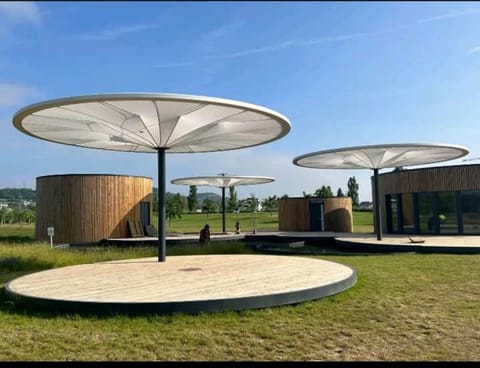 Three large white umbrella shades over a round timber deck on a lawn